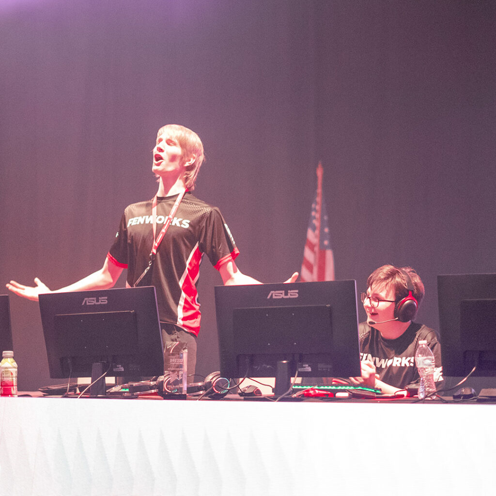 Esports competitor celebrating with a victorious howl after winning a gaming match, with a friend by their side, both sharing smiles and laughter.